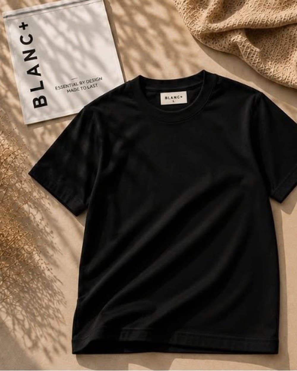 The Blanc+ Essential Tee in Black, laid flat beside a Blanc+ pouch in natural light