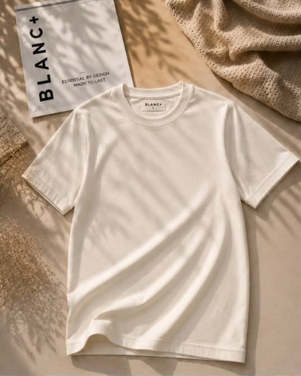 The Blanc+ Essential Tee in Cream, laid flat beside a Blanc+ pouch in natural light