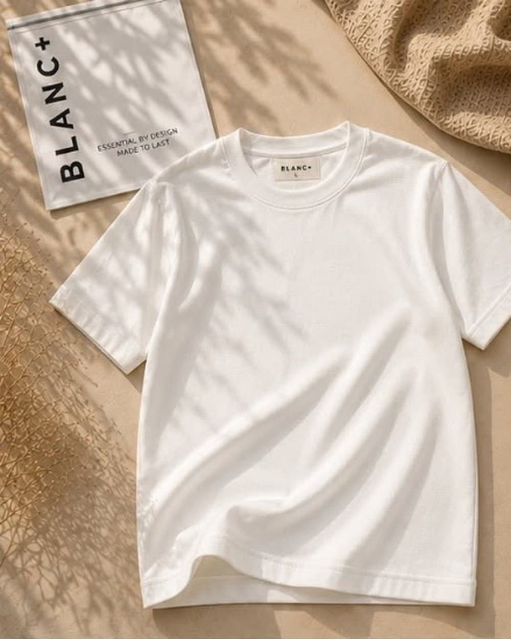 The Blanc+ Essential Tee in White, laid flat beside a Blanc+ pouch in natural light